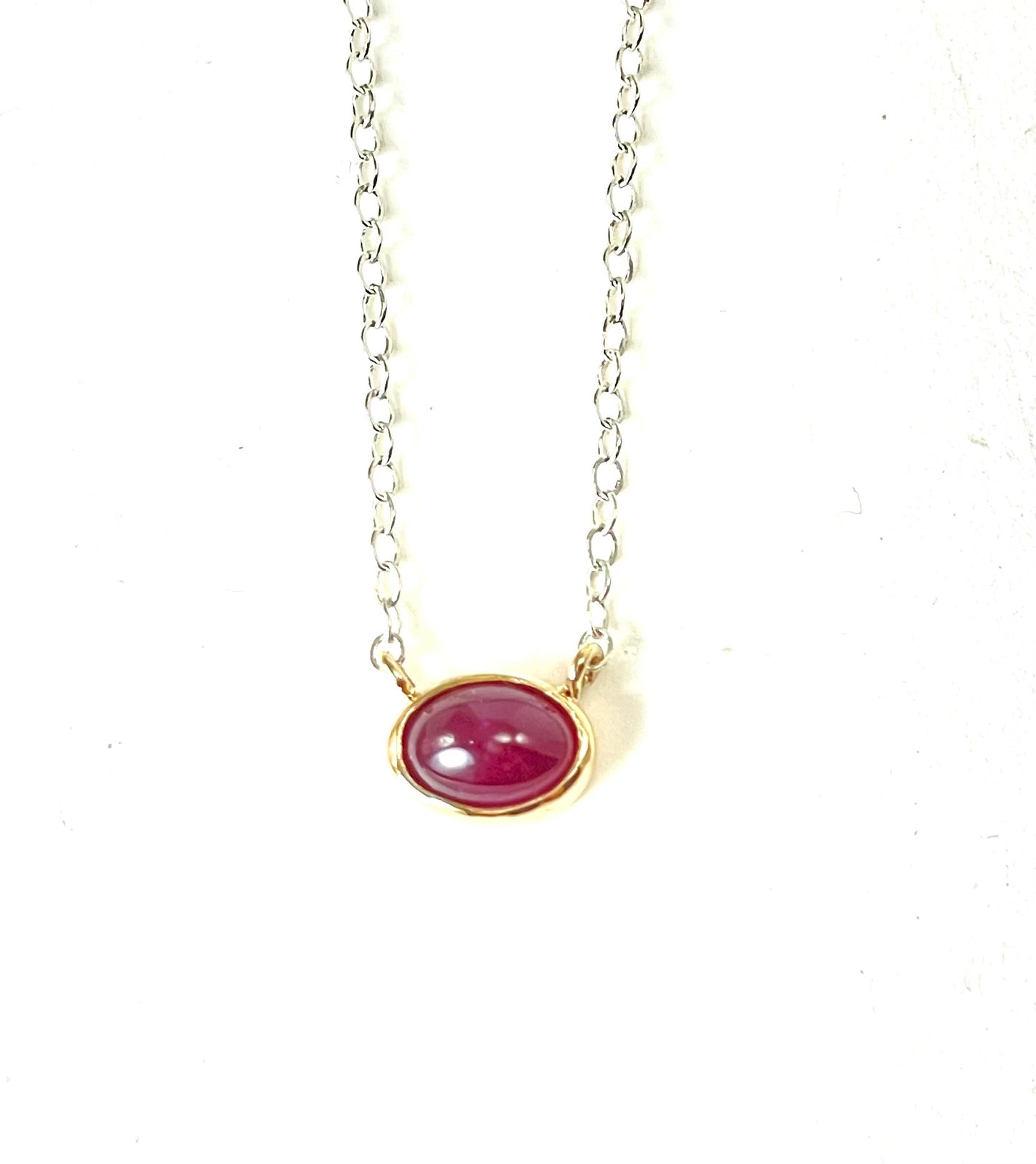 Ruby cabochon set in 14K gold on a silver chain.