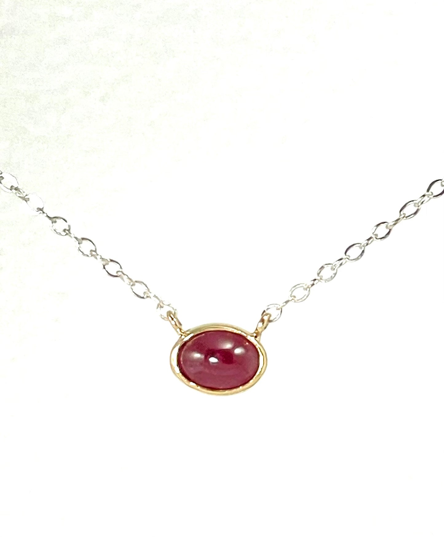 Ruby cabochon set in 14K gold on a silver chain.