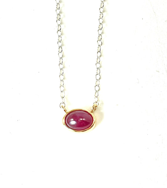 Ruby cabochon set in 14K gold on a silver chain.